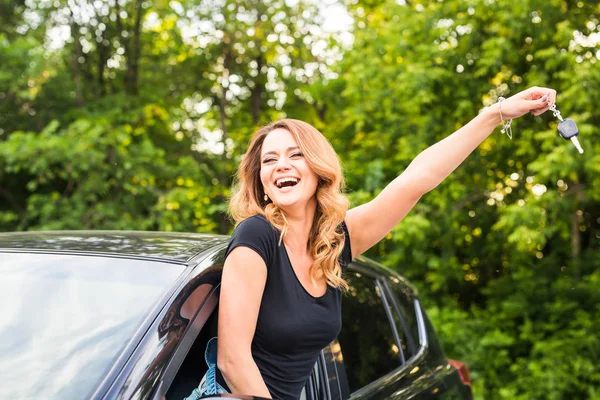 Young happy woman in the car with keys in hand - concept of buying car.