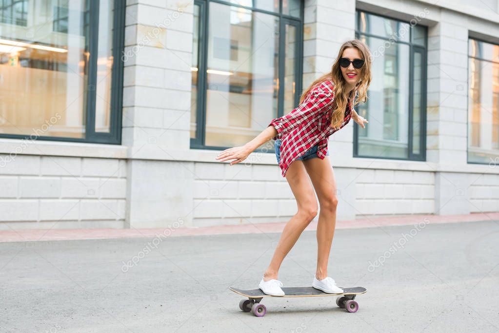 summer holidays, extreme sport and people concept - happy girl riding skateboard on city street