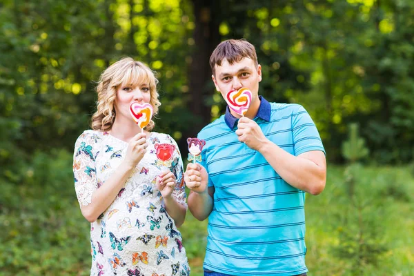 Těhotenství, Rodina, štěstí a zábavný koncept - Man a těhotná žena bavit s candy v parku — Stock fotografie