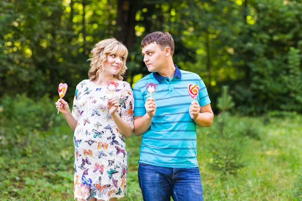 Беременность, семья, счастье и веселье концепция - Мужчина и беременная женщина весело провести время с конфетами в парке — стоковое фото