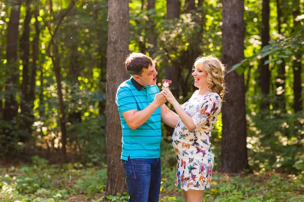 Schwangerschaft, Familie, Glück und Spaßkonzept - Mann und Schwangere haben Spaß mit Süßigkeiten im Park — Stockfoto