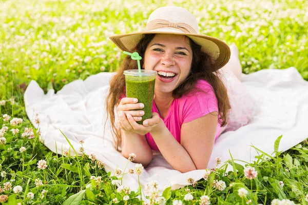 Mujer joven divertirse en el parque y beber batidos verdes en un picnic . — Foto de Stock