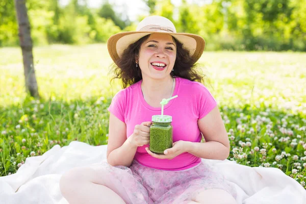 Jonge vrouw veel plezier in het park en het drinken van groene smoothies op een picknick. — Stockfoto