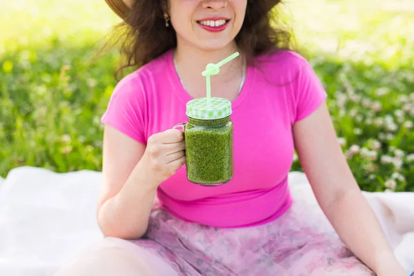 Jonge vrouw veel plezier in het park en het drinken van groene smoothies op een picknick. — Stockfoto