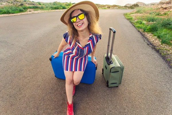 Glückliche Reisende, die auf einem Koffer auf der Straße sitzt und lächelt. Konzept der Reise, Reise, Reise — Stockfoto