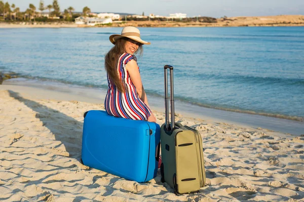 Feliz mulher turista rindo sentado em frente ao mar em mala azul. Viagens e conceitos de férias de verão . — Fotografia de Stock