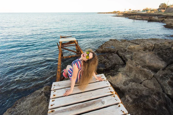 Joven mujer feliz sentada en el muelle de madera y riendo . — Foto de Stock