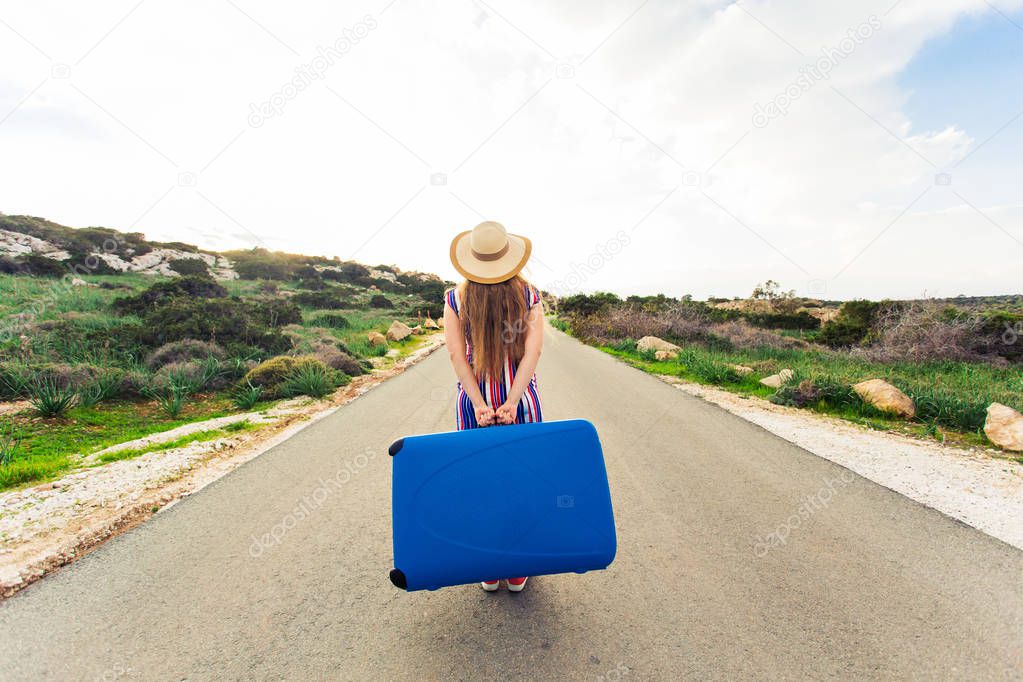 Beautiful young lady travelling with a blue suitcase, rear view