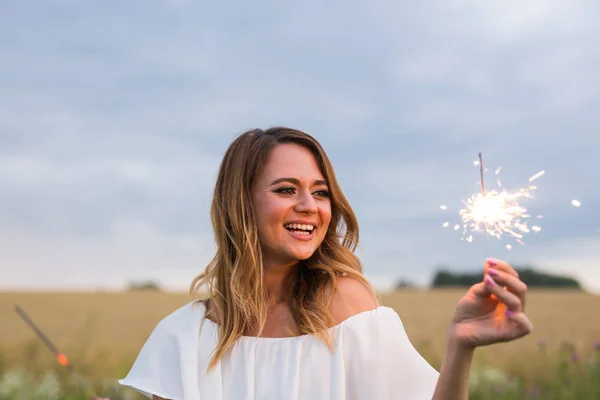 Outdoor photo of young beautiful happy smiling girl holding sparkler. Holidays concept. — Stock Photo, Image