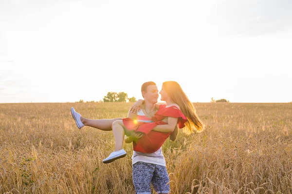 Feliz casal jovem desfrutando no campo de trigo, temporada de verão. Luz do pôr-do-sol, luz do clarão, espaço de cópia — Fotografia de Stock