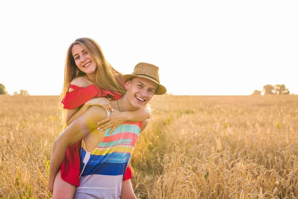 Casal feliz se divertindo ao ar livre no campo de trigo ao pôr do sol. Rindo Família alegre juntos. Conceito de Liberdade. Piggyback. . — Fotografia de Stock