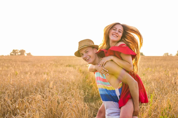 幸せなカップルを持つ楽しいアウトドアで夕日に麦畑。うれしそうな家族を一緒に笑って。自由の概念。ピギーバック. — ストック写真