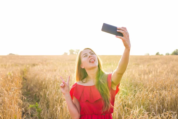 Mladá šťastná žena s úsměvem při pořizování selfie obrázek s mobilním telefonem v poli — Stock fotografie