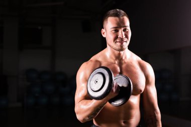 Yakışıklı atletik vücut geliştirici, halterle egzersiz yapıyor. Koyu arkaplanda fitness kaslı vücut