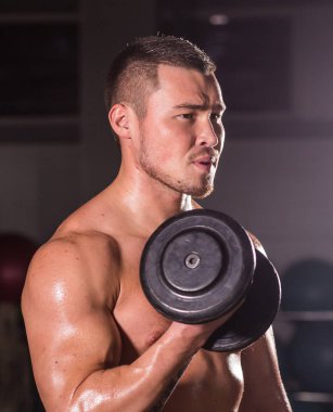 kaslı vücut geliştirmeci biri dumbbells ile yapıyor.