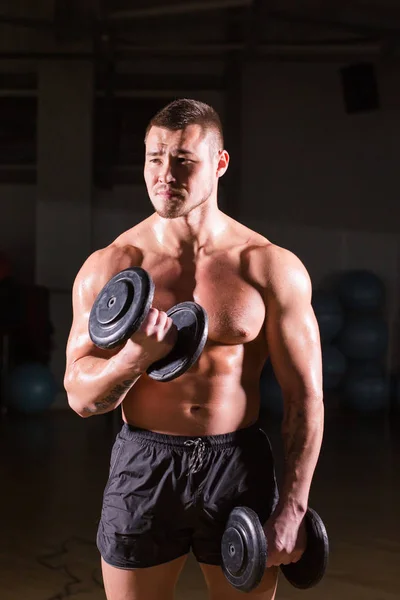 Fešák sportovní chlap kulturista dělá cvičení s činky. Fitness svalové tělo na tmavém pozadí — Stock fotografie