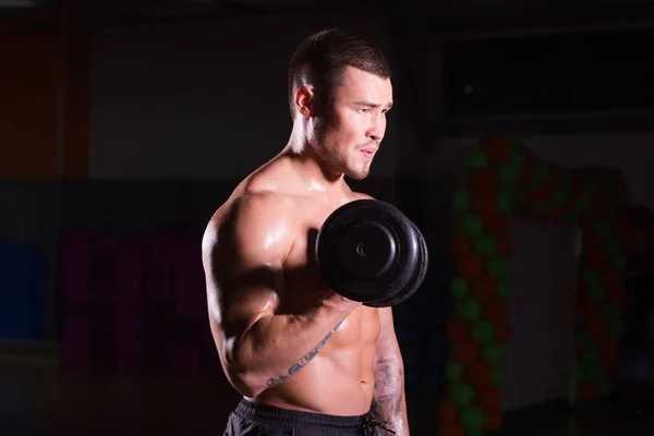 Handsome power athletic guy bodybuilder doing exercises with dumbbell. Fitness muscular body on dark background