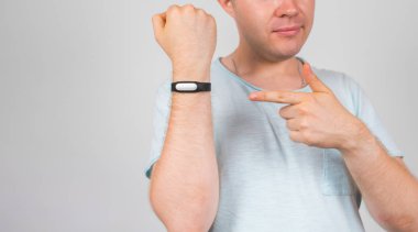 Yakın çekim genç adam ayakta ve gri arka plan üzerinde fitness İzleyicisi'ni işaret