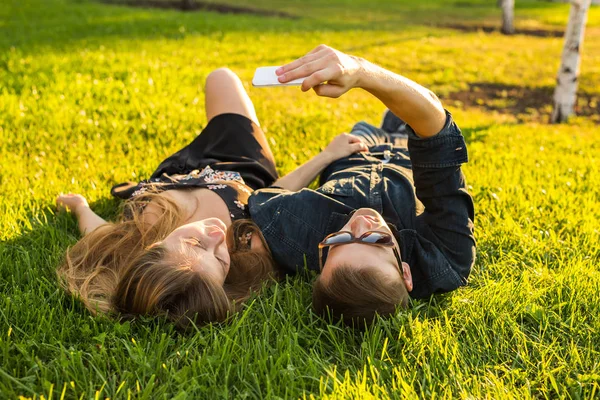 Amor e conceito de pessoas - casal adolescente feliz deitado na grama e tomando selfie no smartphone no verão — Fotografia de Stock