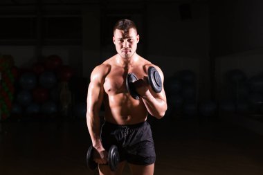 kaslı vücut geliştirmeci biri dumbbells ile yapıyor.