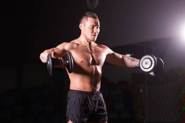 kaslı vücut geliştirmeci biri dumbbells ile yapıyor.