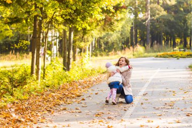 Genç anne sonbahar parkında kızıyla oynuyor..