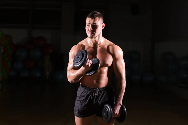 Muskulöser Mann trainiert im Fitnessstudio und macht Übungen mit Kurzhanteln am Bizeps, kräftiger männlicher nackter Oberkörper. — Stockfoto