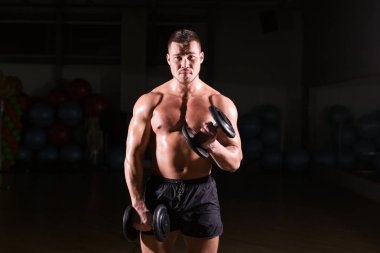 Yakışıklı atletik vücut geliştirici, halterle egzersiz yapıyor. Koyu arkaplanda fitness kaslı vücut