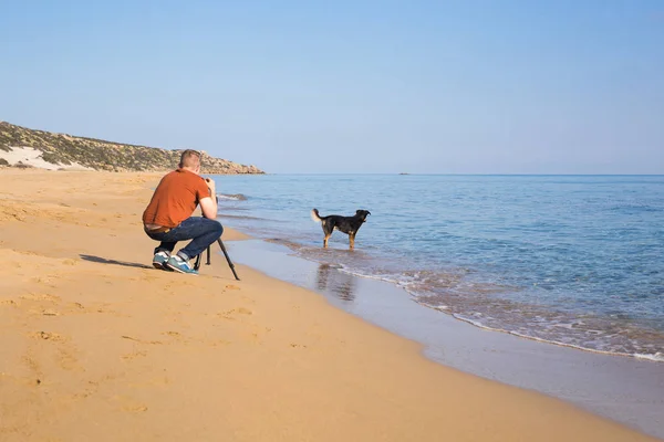 Young photographer and videographer making photos and videos of sea and his dog with the camera on a tripod. Mediterranean sea