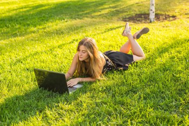 bahar ya da yaz saati parkta yeşil çimenlerin üzerinde dizüstü bilgisayar ile bir güzel öğrenci kız portresi.