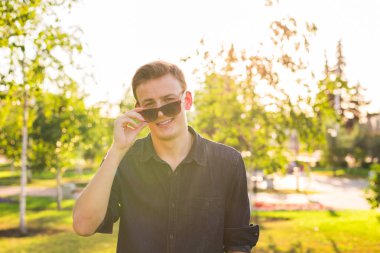 Komik gülümseyen hipster yakışıklı adam şık yaz bez güneş gözlüğü sokakta.