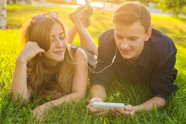 Jeune caucasien charmant couple ou étudiants couchés sur l'herbe ensemble, en écoutant de la musique. Amour, relation, été et style de vie concept — Photo