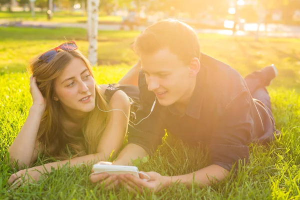 Jovens caucasianos casal encantador ou estudantes universitários deitados na grama juntos, ouvindo música. Amor, relacionamento, verão e conceito de estilo de vida — Fotografia de Stock