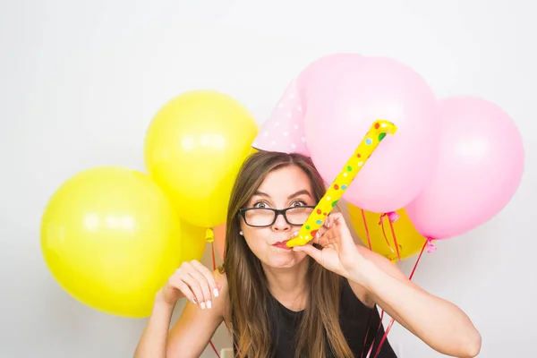 Junge attraktive lächelnde Frau mit Geburtstagshut, Luftballons und Trillerpfeife auf weißem Hintergrund. Feiern und Feiern. — Stockfoto