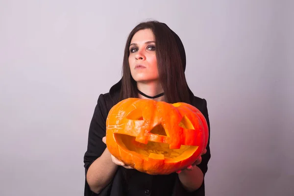 Хэллоуинская ведьма держит в студии оранжевую тыкву Джек о Фонарь — стоковое фото