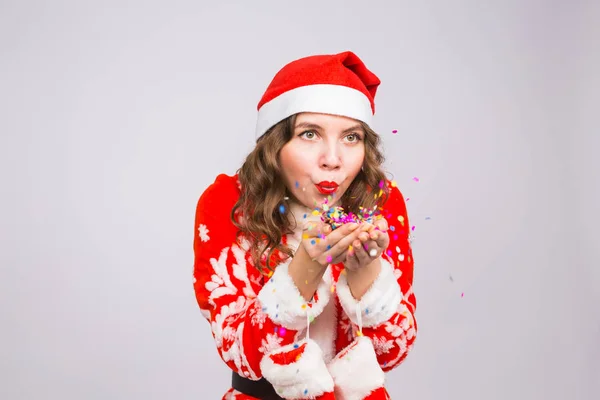 Bella ragazza in costume di Babbo Natale che accoglie il nuovo anno 2018 soffiando coriandoli alla macchina fotografica. Celebrazione di Capodanno e concetto di partito — Foto Stock