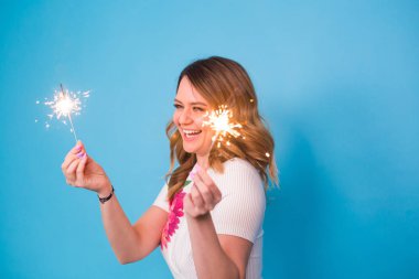 Bengal ışıklar mavi arka plan üzerinde tutan mutlu bir kadın portresi. Noel, kutlamalar ve tatil kavramı