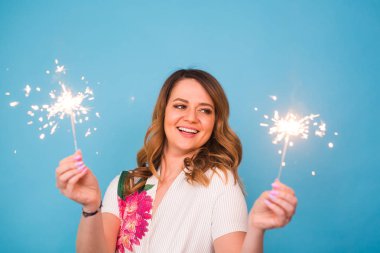 Bengal ışıklar mavi arka plan üzerinde tutan mutlu bir kadın portresi. Noel, kutlamalar ve tatil kavramı