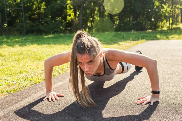Jeune femme en forme faisant de l'exercice en faisant des pompes à l'extérieur — Photo