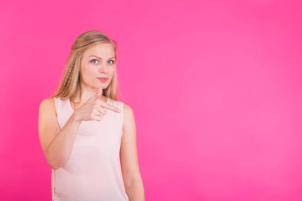 Молода жінка вказує на рожевий фон з копіювальним простором — стокове фото