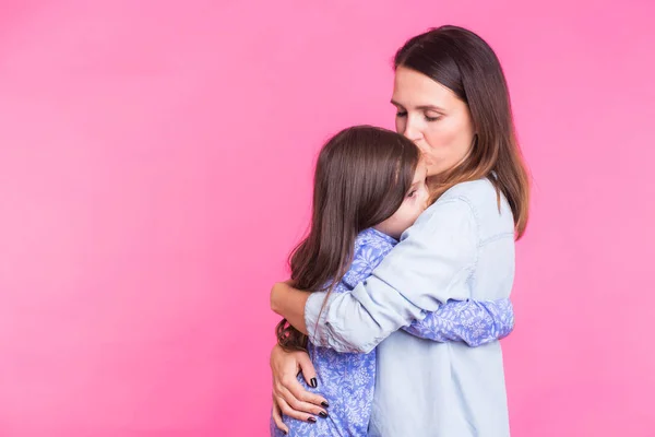 Personas, la felicidad, el amor, la familia y el concepto de maternidad - hija pequeña y feliz abrazando y besando a su madre sobre fondo rosa — Foto de Stock