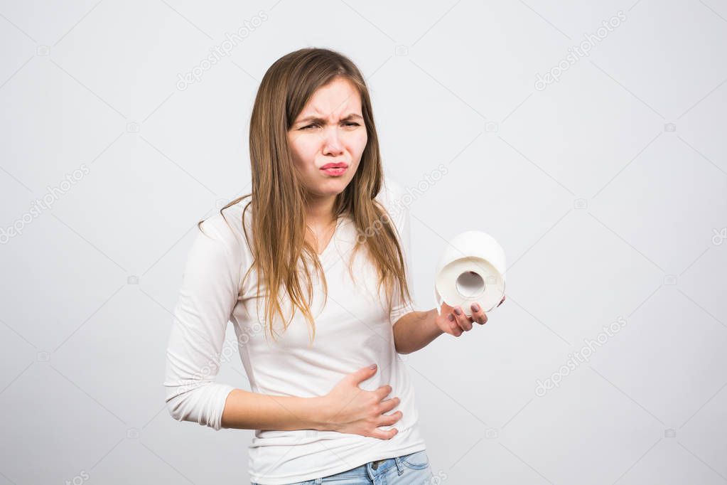 Woman with stomach pain and toilet paper roll on white background
