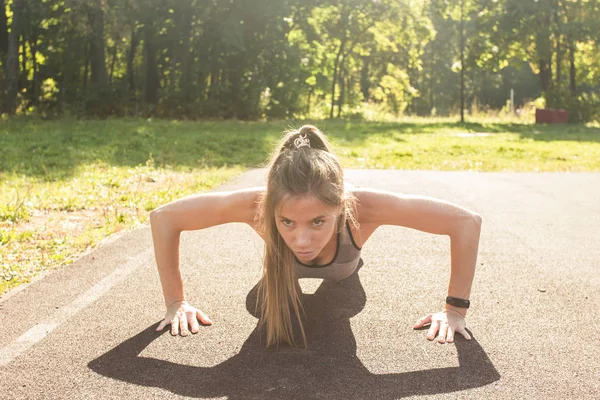 Femme de remise en forme faisant push-ups pendant l'entraînement cross extérieur. Belle jeune et forme physique sport modèle entraînement à l'extérieur dans le parc — Photo