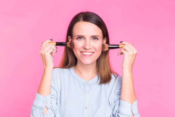 Professionelle Maskenbildnerin mit Pinseln auf rosa Hintergrund — Stockfoto