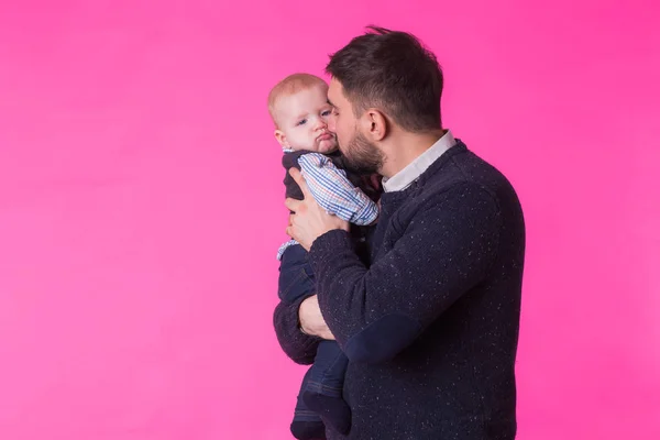 Feliz padre sosteniendo bebé hijo en manos sobre fondo rosa — Foto de Stock