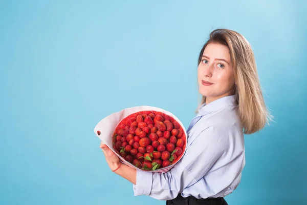 Bouquet of strawberries in the hands of a girl on blue background