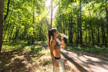 Güneşli bir günde açık havada su içen sportif bir kadın..