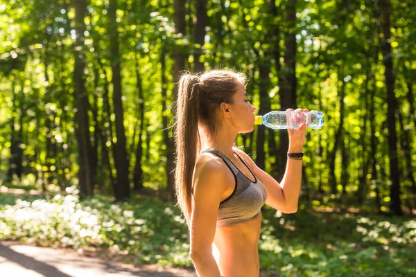 Fitness belle femme buvant de l'eau et transpirant après l'exercice sur la journée chaude d'été dans le parc. Athlète féminine après l'entraînement . — Photo