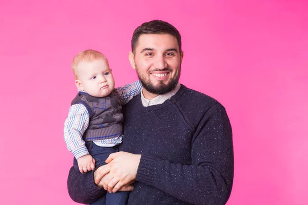 Feliz padre sosteniendo bebé hijo en manos sobre fondo rosa — Foto de Stock