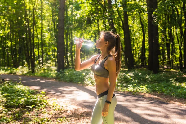 Fitness belle femme buvant de l'eau et transpirant après l'exercice sur la journée chaude d'été dans le parc. Athlète féminine après l'entraînement . — Photo